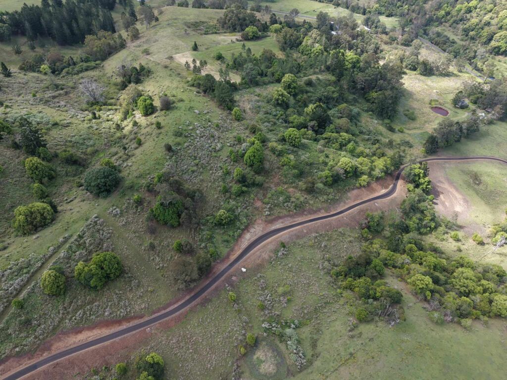 Aerial view of a newly constructed paved road winding through a green rural landscape.